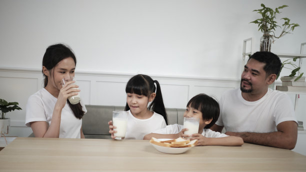一个亚洲泰国家庭喝着新鲜的白牛奶和面包一起欢乐。图片下载