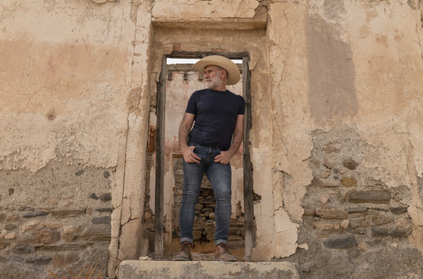 戴牛仔帽的成年男子站在废弃建筑的门口图片下载