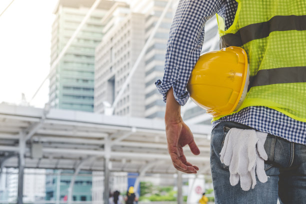 工程师手拿安全帽白色工作头盔，为土木建筑工程安全帽。在工地上，身穿安全服的建筑工程师手持白色工作头盔和安全帽图片下载