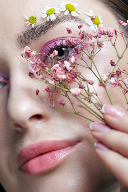 女性的脸，粉色的妆容。一名女子，手里拿着凤仙花，近脸。眉毛上点缀着小的洋甘菊花。图片下载