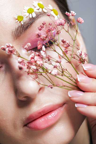 女性的脸，粉色的妆容。一名女子，手里拿着凤仙花，近脸。眉毛上点缀着小的洋甘菊花。图片下载