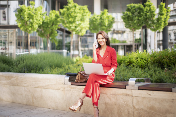 一位自信的女士正在接听电话，坐在户外使用笔记本电脑图片下载