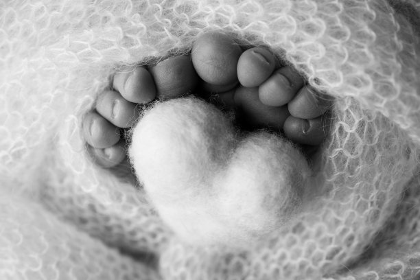 新生儿的小脚。羊毛毯里新生儿柔软的脚。一个新生儿的脚趾，脚跟和脚的特写。在婴儿的腿上编织心。微距摄影。黑色和白色。图片下载