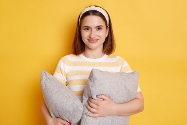 画像年轻微笑的梦想快乐的女人在睡眠眼罩休息放松在家里抱着枕头摆出孤立的黄色背景，好心情，晚上，睡觉。图片下载