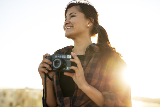美丽的女人拿着相机在美丽的地方拍照。图片下载