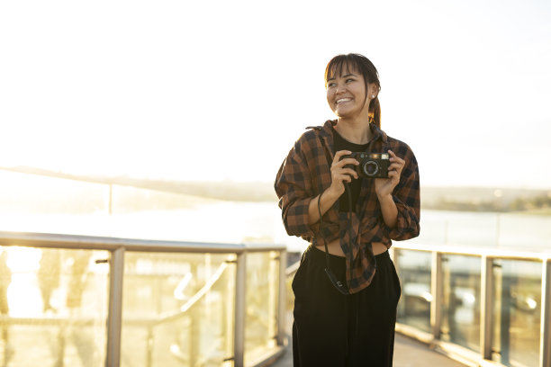 美丽的女人拿着相机在美丽的地方拍照。图片下载
