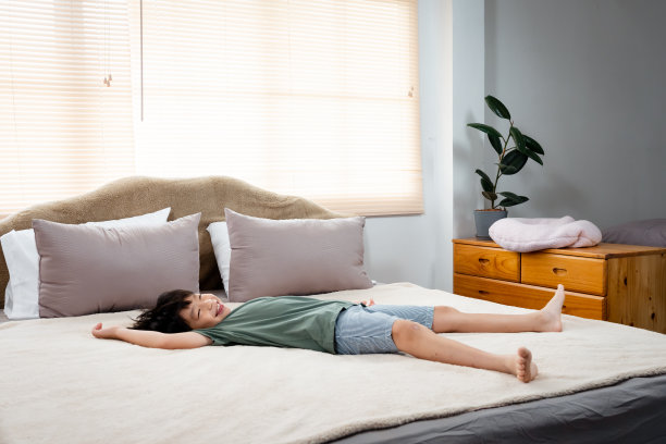 英俊的亚洲男人穿着一件绿色t恤..睡觉，舒服地伸展你的腿。在房子卧室里柔软的床上快乐地躺着图片下载