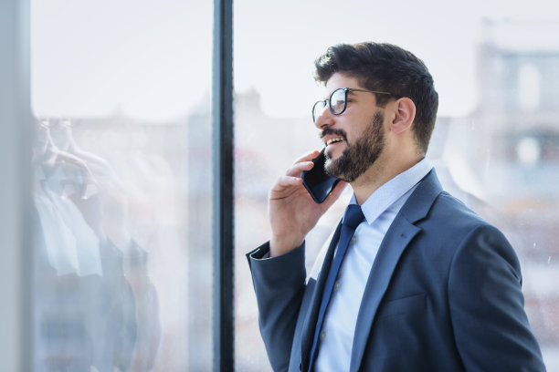 商人站在办公室靠窗的地方打电话图片下载