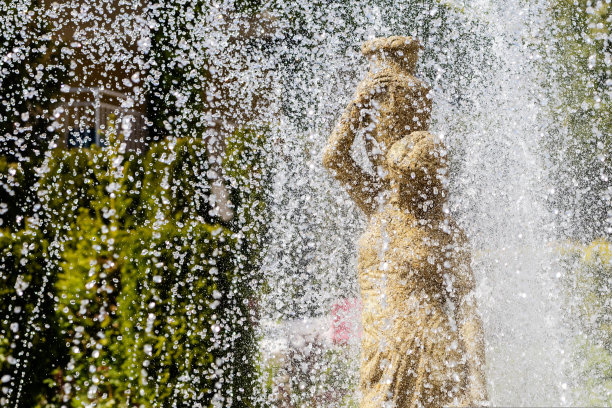 近景喷泉倾泻在一个女人的雕像上。水花四溅，石雕一个拿着水壶的女孩图片下载