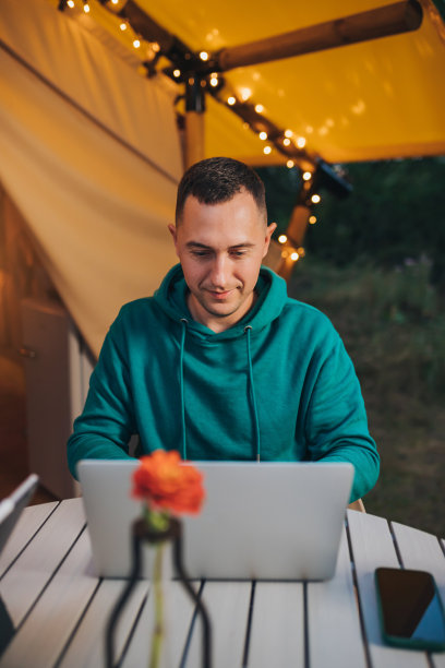 快乐的人自由职业者使用笔记本电脑在一个舒适的野营帐篷在一个夏天的晚上。户外度假度假的豪华露营帐篷。生活方式的概念图片下载