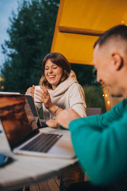 幸福的家庭夫妇自由职业者在一个舒适的野营帐篷在夏天的晚上使用笔记本电脑。户外度假度假的豪华露营帐篷。生活方式的概念图片下载