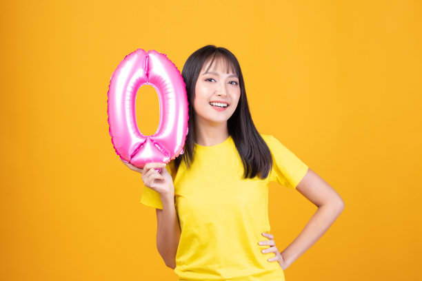 新年快乐和圣诞快乐的概念。年轻漂亮的亚洲女人，黄色背景上有0号气球。图片下载