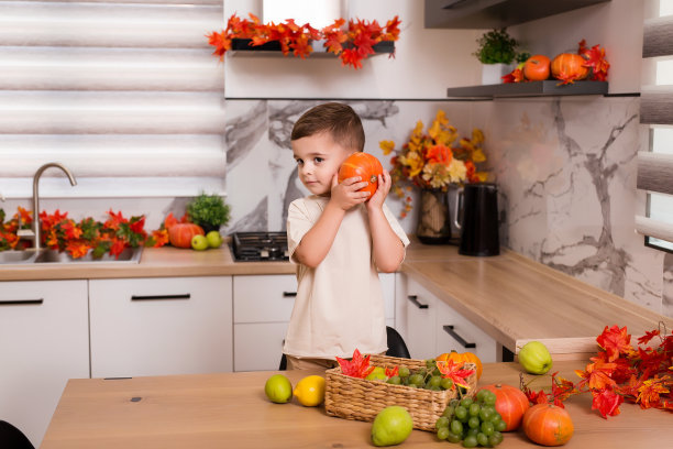 微笑可爱的男孩站在柜台水果，秋叶和南瓜。秋季装修厨房。假期的概念。图片下载