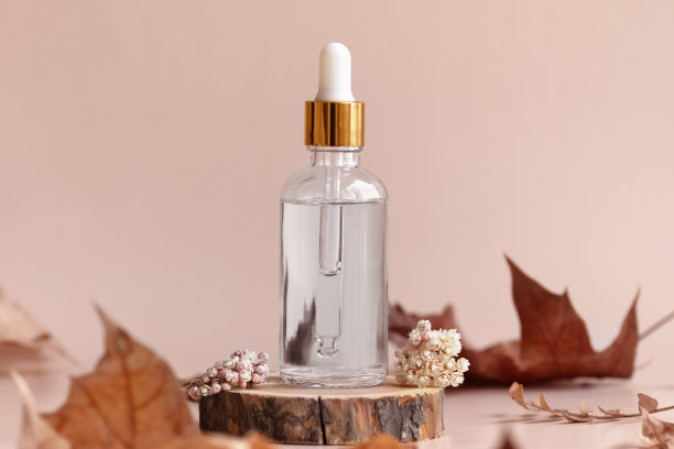 透明玻璃化妆品滴管瓶站在木圆盘与干花和叶子。秋天的成分图片下载