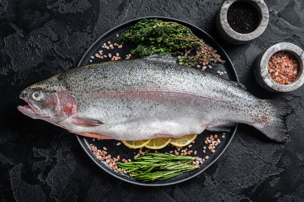 生鳟鱼，新鲜的鱼配上香草。黑色背景。俯视图图片下载