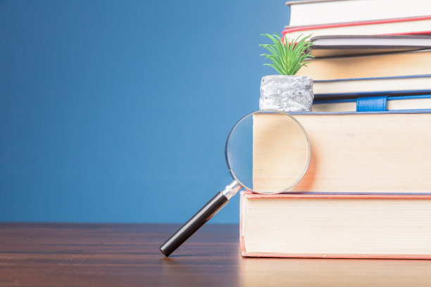在学校信息图书馆的木桌上堆放放大镜的书籍，教育、阅读、学习的概念，蓝色背景的拷贝空间。图片下载