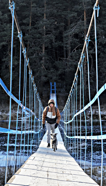 年轻男子带着混合品种的毛毛狗走在木桥上覆盖着初雪和冰的河流在秋天或初冬徒步旅行和宠物积极的生活方式狗收养图片下载