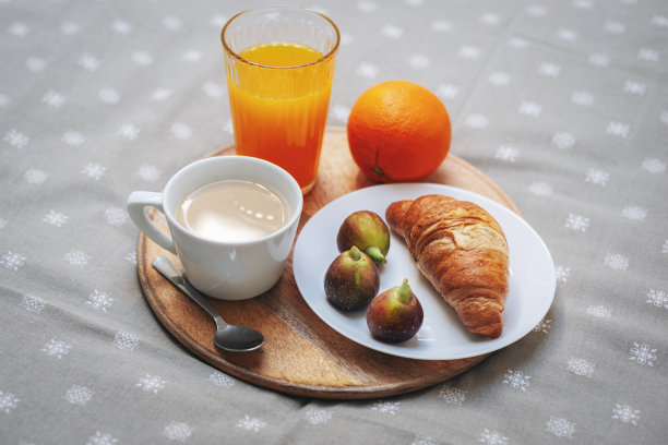 早上好，美味的早餐在床上。牛角包放在盘子里，有无花果，咖啡杯，橙汁和一个橙子放在托盘里。近距离图片下载