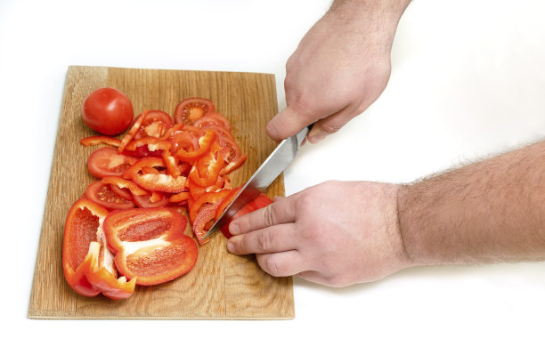 特写男子的手，切新鲜成熟的西红柿和辣椒与刀在木材砧板上在家里的厨房图片下载