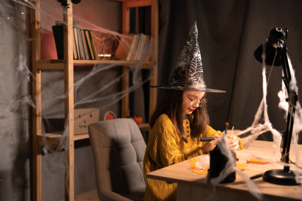 可爱快乐的小女巫准备万圣节，画可怕的脸在南瓜上，坐在家里的桌子，微笑的孩子做杰克灯。节日装饰图片下载