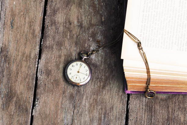 一张旧木桌上放着一块古董怀表和一本旧书图片下载