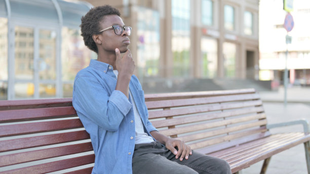 沉思的非洲青年坐在户外长凳上思考图片下载