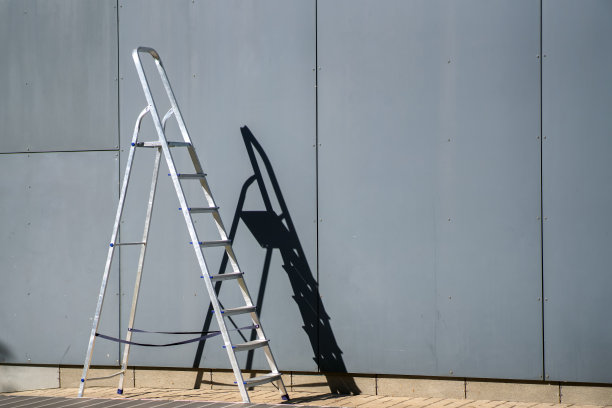 一个铝制的梯子立在灰色的金属墙旁边图片下载