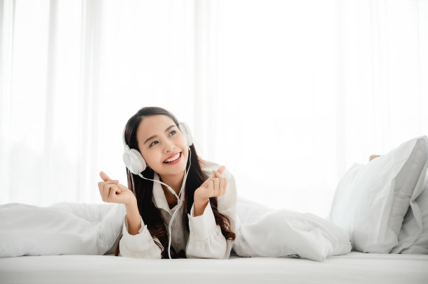 美丽年轻的亚洲女人戴着耳机听音乐，躺在床上在卧室的早上时间图片下载