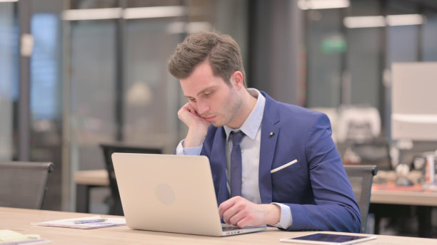 疲惫的商人在办公室用笔记本电脑打盹图片下载