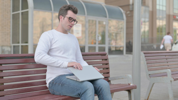 年轻男子关闭笔记本电脑后离开长凳图片下载