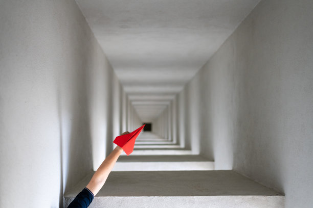 手持红色折纸飞机通过木制框架飞行。图片下载