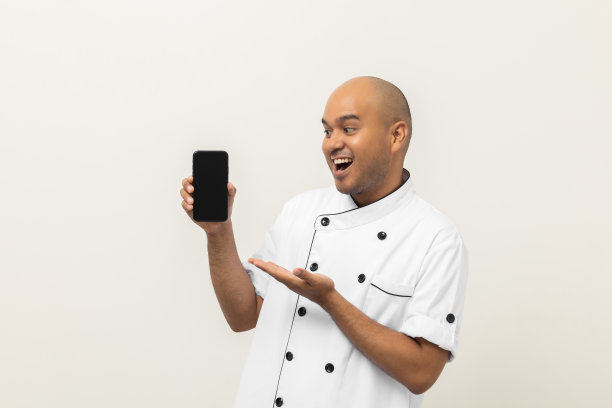 年轻的亚洲男厨师展示空屏幕的手机，选择各种美味的菜肴菜单，好口味的顾客点菜。网上智能手机送餐，购买各种菜肴图片下载