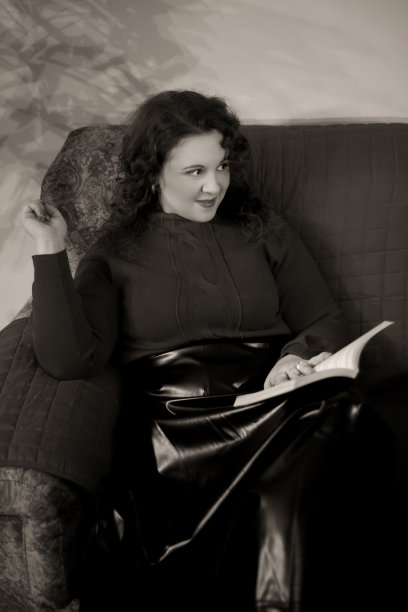 年轻美丽的女人画像坐在沙发上，手里拿着书，对着人微笑图片下载