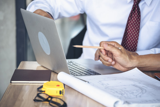 承包商施工工程师在施工办公室现场的建筑师桌子上开会交谈。商人、工程师、经理与工头讨论，团队建设者看计划蓝图笔记本电脑图片下载