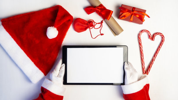 圣诞老人手里拿着一块平板电脑。礼物盒。图片下载