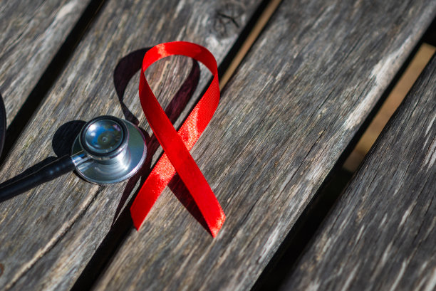 AIDS红丝带，听诊器平放于木面上。象征着艾滋病和艾滋病毒的一天。艾滋病毒控制的概念。在户外拍摄。副本的空间。图片下载