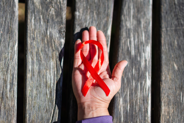 女性手中拿着红丝带，宣传艾滋病。世界艾滋病日的概念。妇女的手支持世界艾滋病日和国家艾滋病毒、艾滋病概念。木质表面。前视图。图片下载