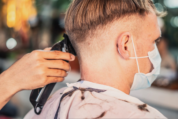 生活照片理发店。年轻的男顾客戴着口罩，侧面背部后视图。理发师男手工动梳子工具电动剪刀。现代短发。时尚服务沙龙图片下载