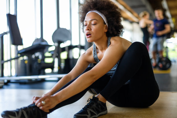 年轻的运动黑人妇女系鞋带，而坐在地板上的健身房。图片下载