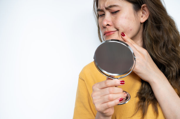 画像的亚洲妇女担心她的脸，当她看到的问题痤疮炎症发生在她的脸上的迷你镜子。图片下载