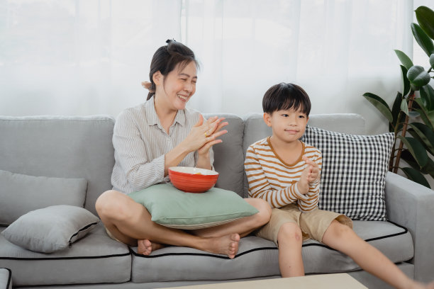 一位单身母亲和她的亚裔儿子坐在客厅的沙发上看电视欢呼。母女二人在心爱的球队获胜后表达了她们的喜悦之情。图片下载