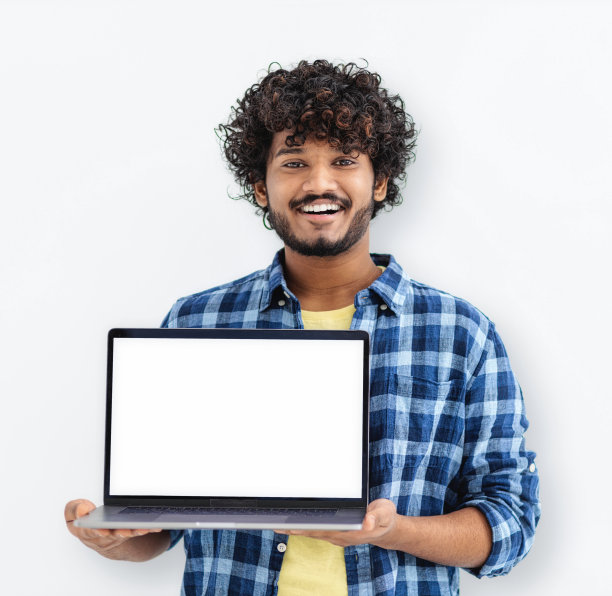 快乐的印度男学生站在打开的笔记本电脑上，白色背景上有空白的白色模型屏幕，看着相机微笑图片下载