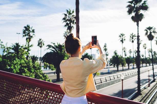 千禧一代女博主的后视图，用手机拍摄城市风景如画的场景，连接4g无线网络，用于在线浏览和网络，度假旅行时间图片下载