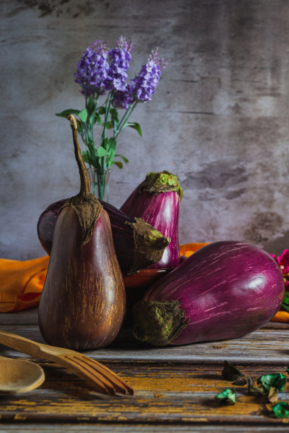 一张木桌上有条纹茄子的静物照片，旁边放着一些木制餐具和一块橙色的布。图片下载