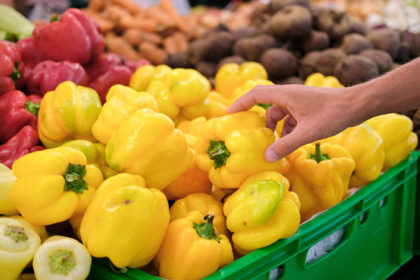 一个男人在商店柜台上挑选一种黄色的辣椒。蔬菜,收获。图片下载