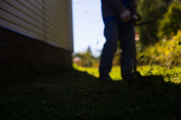 男子在后院用电动或汽油割草机割高草。园艺护理工具和设备。用手动割草机修剪草坪的过程图片下载