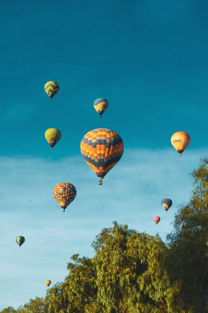 彩色热气球在树木之间的天空中飞行，享受着自由和大自然的风景，这是一场不可思议的冒险图片下载