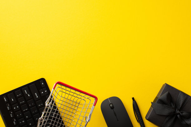 黑色星期五的促销概念。顶视图照片黑色礼盒带蝴蝶结，购物车笔，电脑鼠标和键盘上孤立的黄色背景与空白图片下载