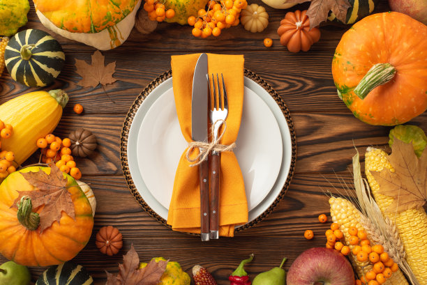 感恩节的概念。俯视图照片盘刀叉餐巾生蔬菜南瓜苹果玉米西葫芦pattypans小麦罗文枫叶在孤立的深色木桌背景图片下载