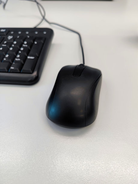 白色办公桌上一只没有牌子的黑色有线鼠标图片下载